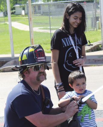 Burnet Fire Department Engineer Travis Tschoerner assists as pre-school child Jeremiah Chavez squeezes a fire house in Burnet at the Head Start center. Burnet High School sophomore Gabriela Chavez encourages her young brother. Raymond V. Whelan/Bulletin