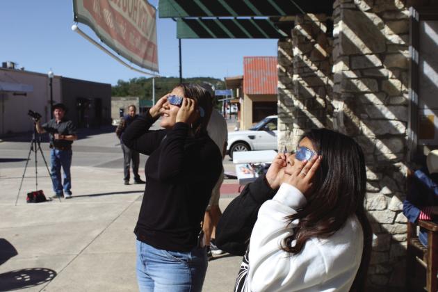 (Left) Burnet resident Gina Ramirez and her daughter Ashley see the partial eclipse during the Annular Eclipse Party Oct. 14 in Burnet at the Herman Brown Free Library. Behind Gina (left) Burnet resident Bret Hyder steadies his Nikon camera for photographs of the eclipse. Behind Hyder, Austin visitor Sunjit Tara enjoys the party. Photos by Raymond V. Whelan/Bulletin