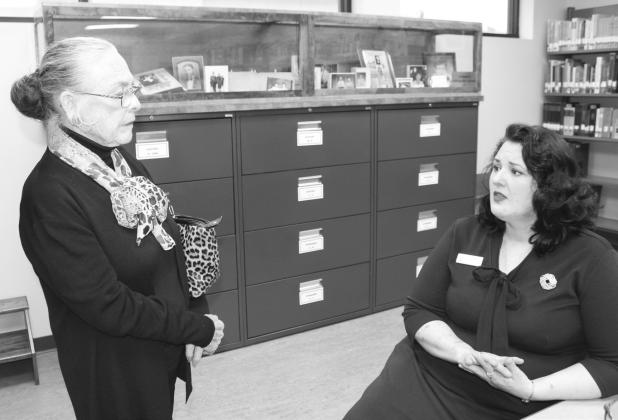 Janie Cozby listened to Herman Brown Free Library Director Florence Reeves (seated) discuss new fixtures for the library genealogy center. Behind the pair, one display case is dedicated to the memory of Judith “Judy” Kuykendall. Photos by Raymond V. Whelan/Bulletin